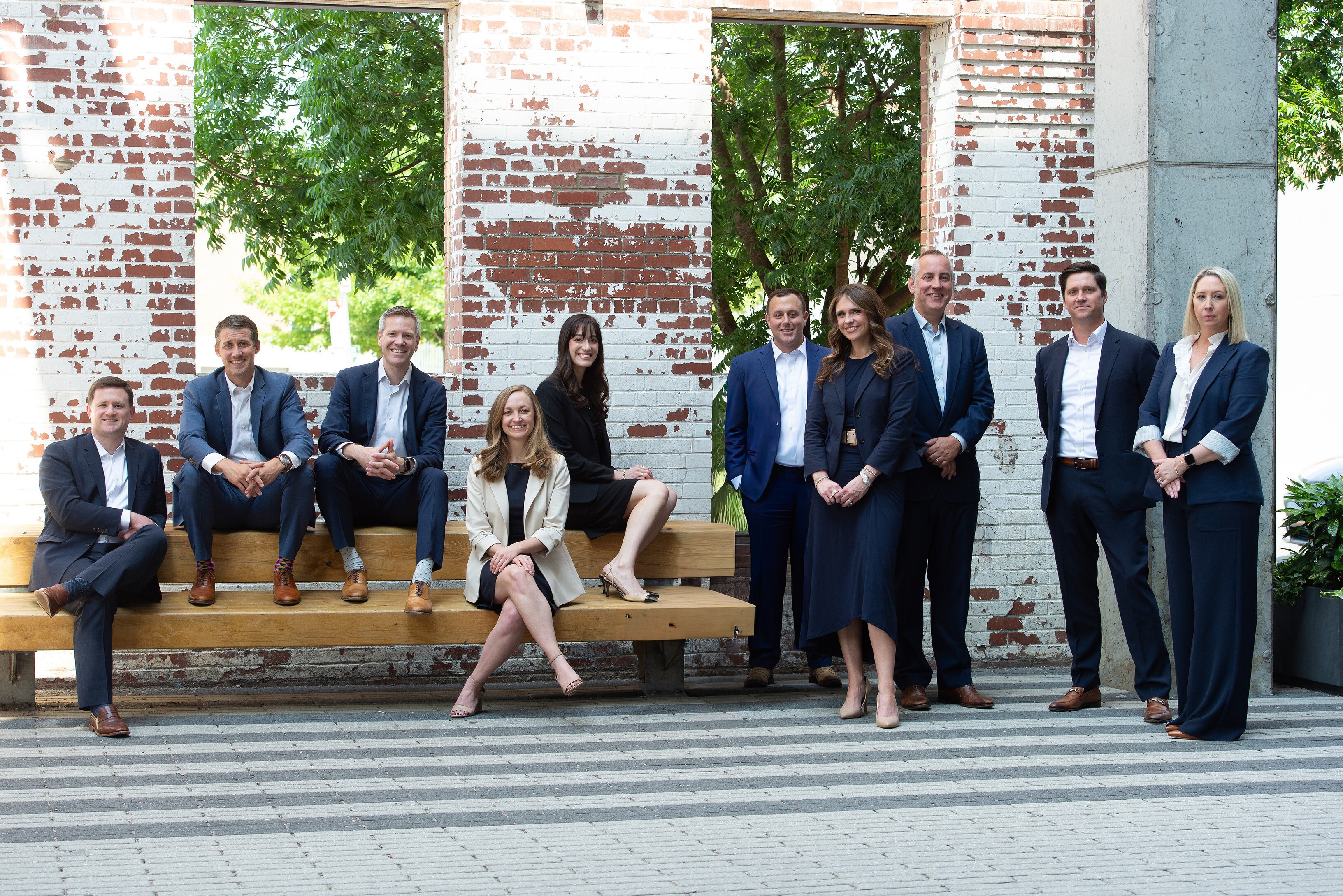 The Lee Segui team sitting on a bench and standing in front of a brick wall